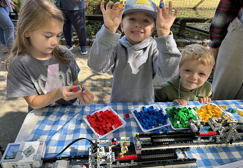 Three young children are engaged in a LEGO sequencer activity.